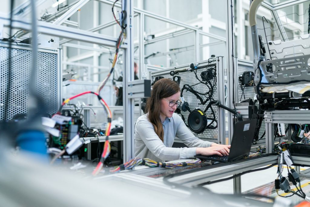 A woman working on a laptop computer in a manufacturing setting.